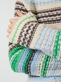 Gebreide trui met horizontale strepen in blauw, crème, bruin en groen, met een gestructureerd patroon. De mouwen zijn breed en ribbelig.