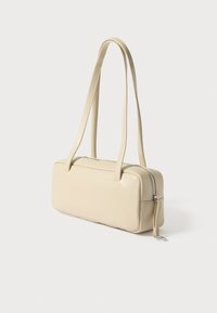 Τσάντα χειρός από κρεμ δέρμα με ορθογώνιο σχήμα, φερμουάρ και δύο ιμάντες για τον ώμο. Διαθέτει μικρό φούντα στο φερμουάρ.