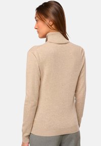 Pull encolure cheminée beige clair en tricot doux, avec des manches longues, un col côtelé et une coupe près du corps.