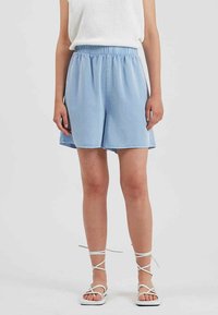 Shorts bleu clair, jusqu'aux genoux, avec une taille élastique, en tissu doux. Assortis avec des sandales blanches à lanières et un haut en tricot texturé.