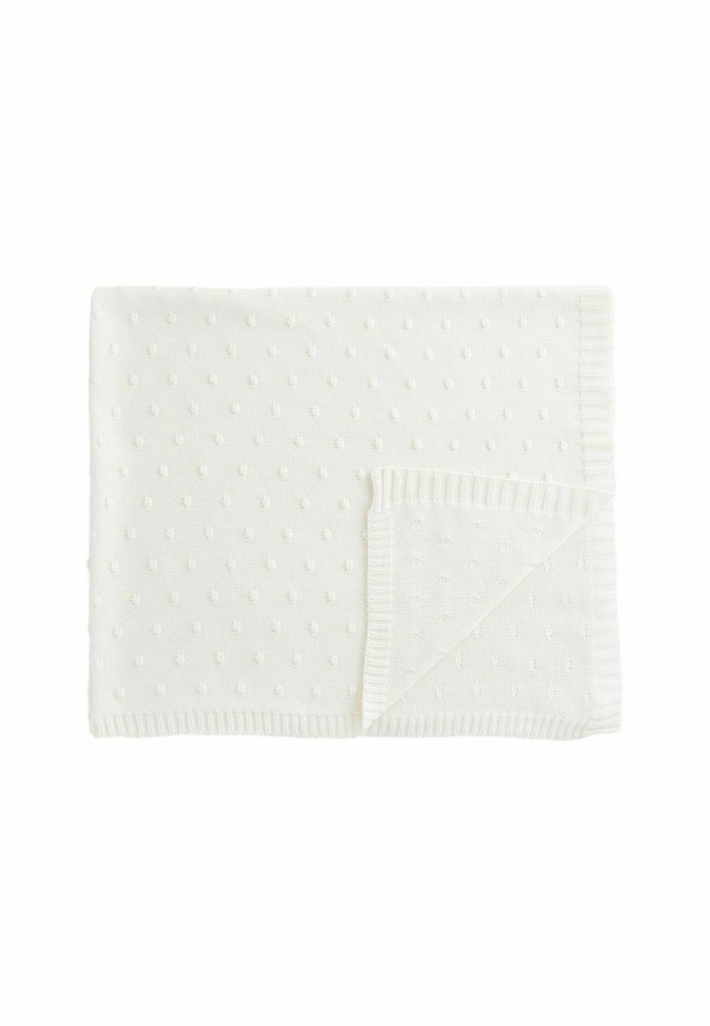 White knitted blanket featuring a textured polka dot pattern, with a ribbed edge along one side. Soft fabric material provides warmth.