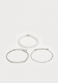 Trois bracelets : un bracelet en perles de verre, un bracelet en chaîne plate en argent et un bracelet délicat en maillons d'argent avec de petites croix en accent.