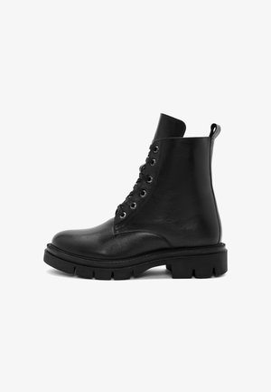 Bottes chelsea en cuir noir avec un bout rond, un laçage à l'avant et une semelle en caoutchouc épaisse. Présente une languette sur le côté et une texture lisse.