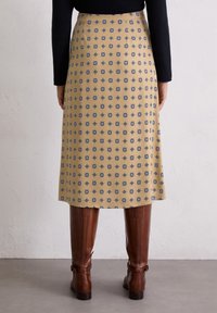 Jupe jaune ornée de motifs géométriques bleus et noirs compliqués, avec une coupe droite et un ourlet juste au-dessus du genou, associée à des bottes brun hautes jusqu'au genou.