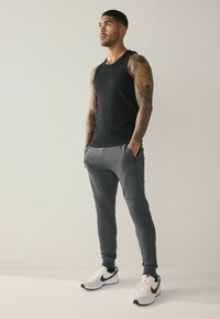 Black tank top, grey joggers with pockets, and white athletic shoes. Features include athletic fit and textured patterns on joggers.