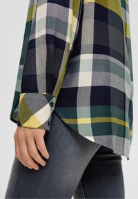 Flannel skjorte i marineblå, grøn og gul ternet. Har knapmanchetter og buet søm. Båret med mørkegrå jeans for et afslappet look.