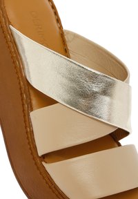 Lichtbeige slipper sandaal met een metallic gouden kruisband, synthetisch materiaal en een bruine rubberen zool. Glad oppervlak met gestikte details.