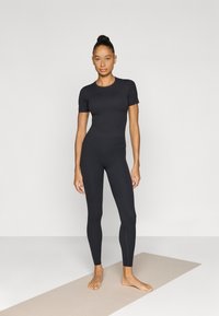 Μαύρο εφαρμοστό τοπ με κοντά μανίκια και κολάν ψηλόμεσο από ελαστικό υλικό, μήκος μέχρι τους αστραγάλους, με λεία υφή, χωρίς ορατά σχέδια ή διακοσμητικά στοιχεία.
