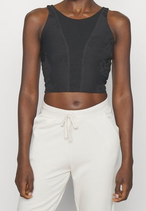 Front view of person wearing a black sleeveless crop top with subtle floral details and white drawstring sweatpants.