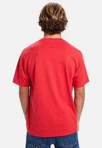 Camiseta de algodón roja con corte relajado, mangas cortas y cuello redondo, que presenta un color sólido sin logotipos ni patrones visibles.