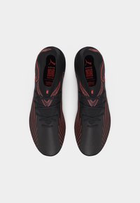 Ζευγάρι μαύρα αθλητικά παπούτσια με κόκκινες λεπτομέρειες και λογότυπο Puma, σε θέα από πάνω σε λευκό φόντο.