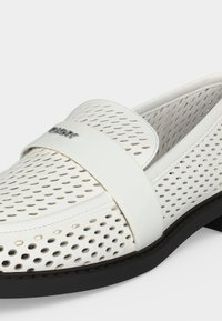 Mocassin en cuir blanc perforé avec semelle noire, bride lisse sur le dessus et petit logo métallique DKNY sur la bride.