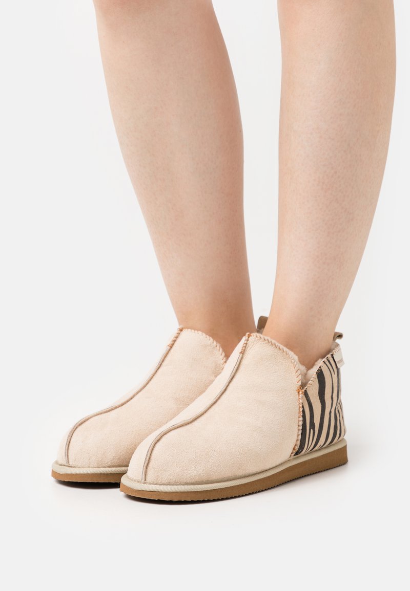 Scarpe slip-on beige realizzate in morbida suede con un lato a motivo zebra testurizzato, dotate di suola in gomma tan e dettagli di cucitura a contrasto.