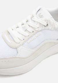 Adidași albi care combină materiale din plasă și piele întoarsă, cu vârful rotund, șireturi plate și un mic accent metalic pe lateral.