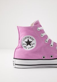 Růžové plátěné vysoké tenisky s bílými očky, černou podrážkou a kruhovou nášivkou s černou hvězdou a textem.