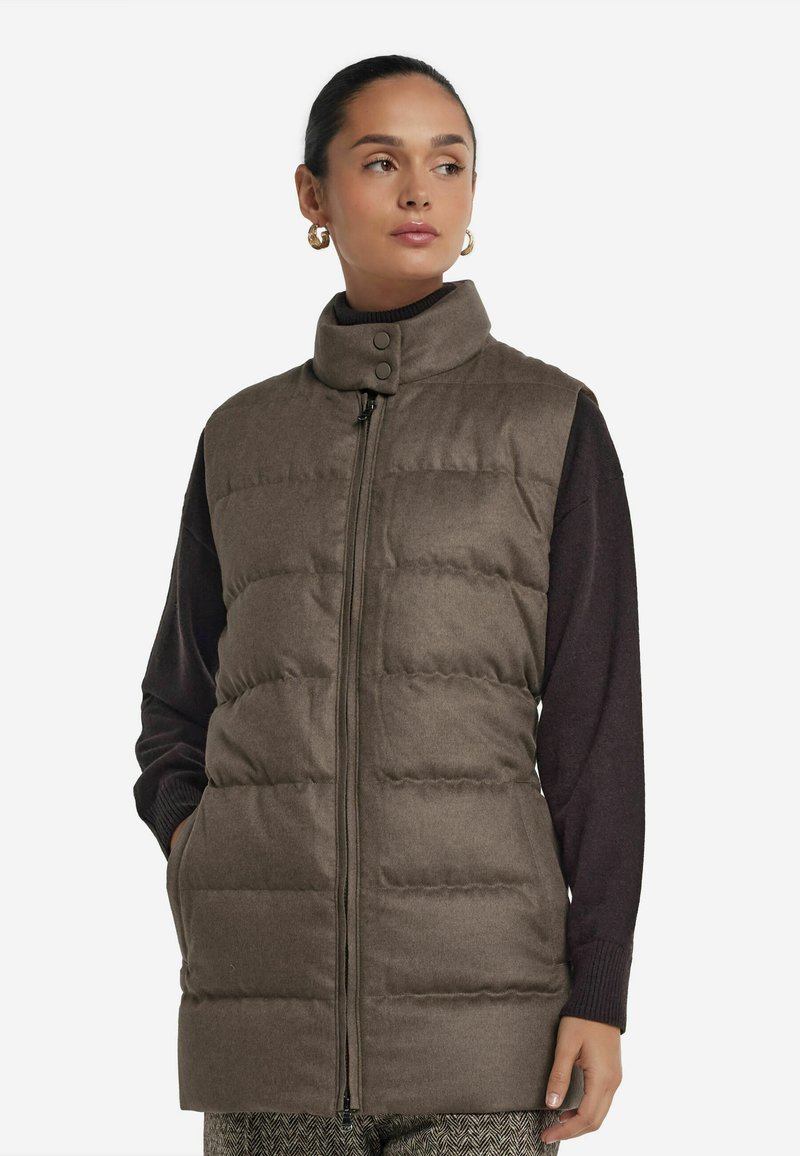 Lång brun puffväst med hög krage, framtida dragkedja och tryckknappar. Har en quiltad design och sidofickor.