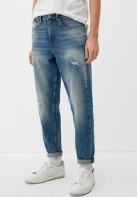 Jean de mezclilla azul claro con corte recto, que presenta detalles desgastados y decoloración. Los dobladillos enrollados revelan calcetines blancos y zapatos.