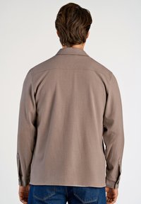 Brun långärmad skjorta med en slät textur, krage och knäppta manschetter, kombinerad med blå denimjeans.