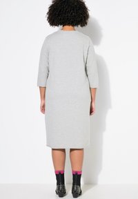 Robe en coton grise à manches trois quarts et décolleté arrondi, arrivant au mollet. Portée avec des bottes chelsea noires à clous et des chaussettes roses.