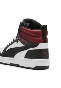 Zwart-witte high-top sneakers met rode accenten. Textuurleer bovenwerk, gevoerde kraag en rubberen zool. Logo op de zijkant en de hak.