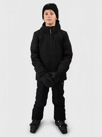 Αγόρι φορώντας μαύρο χειμερινό μπουφάν, παντελόνι, γάντια, καπέλο και μπότες σκι, στέκεται με τα χέρια του σταυρωμένα μπροστά σε απλό φόντο.