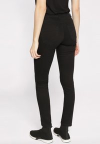 Jean skinny noir avec une texture lisse, doté de deux poches arrière et d'une coupe slim. Porté avec des bottines noires à bout arrondi avec une semelle blanche.