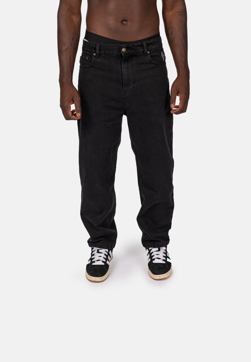 Svarta denimjeans med rak passform, med knappstängning, fem fickor och synlig sömnad. Bärs med svartvita sneakers.