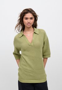 Maglione corto a maniche corte di colore verde chiaro, a maglia, con scollo a V e motivo traforato. Dettagli a coste sul colletto e sull'orlo, vestibilità rilassata.