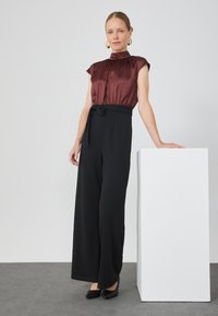 Bordo satenska bluzica s visokim ovratnikom, uparena s crnim širokim hlačama koje imaju pojas s čvorom. Crne visoke potpetice upotpunjuju cijeli outfit.