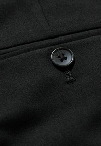 Svart tyg med en slät yta som har en fyra-håls knapp och synliga sömnadsdetaljer. Närbild framhäver materialets kvalitet.