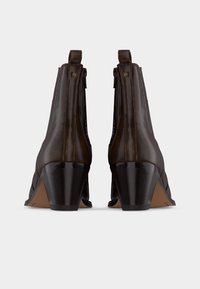 Ζευγάρι από σκούρα καφέ δερμάτινες μποτάκια αστραγάλου με χοντρά τακούνια, φωτογραφημένα από πίσω σε απλό λευκό φόντο.