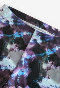Leggings avec un imprimé galaxie dans des nuances de violet, bleu et noir. Tissu lisse avec une ceinture large et des coutures plates.