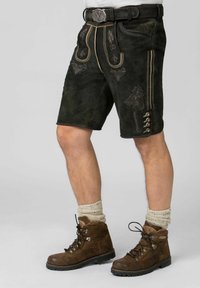 Des shorts en cuir noir présentent une broderie élaborée, des coutures contrastées et des boutons décoratifs. Associés à des bottes marron et des chaussettes beige texturées.