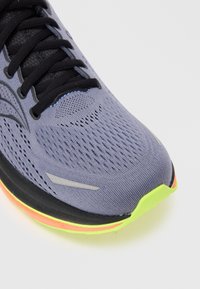 Purple athletic shoe featuring a breathable mesh upper, black laces, reflective silvery accents, and a multi-colored sole with neon green and pink details.