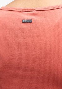 Κοντινό πλάνο ύφασματος σε κοραλί ροζ με μια μικρή μαύρη ετικέτα της μάρκας Columbia ραμμένη κοντά στη ραφή του ώμου.