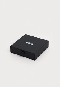 Cutie neagră rectangulară cu o textură mată netedă, având un logo argintiu "BOSS" pe partea de sus și un mic tab pentru deschidere.