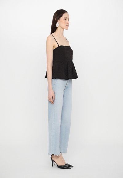 Black peplum top with thin straps, textured fabric, paired with light blue high-waisted jeans and pointed black heels.