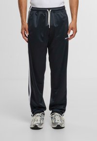 Sötétkék sport futópants, fehér oldalsávokkal, elasztikus derékkal, húzózsinórral és logó részlettel a bal combon; sima szintetikus anyag.