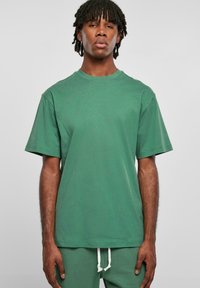 Tricou verde cu mânecă scurtă, fabricat din bumbac, cu decolteu rotund. Prezintă o croială confortabilă și o textură netedă, purtat împreună cu pantaloni asortați.