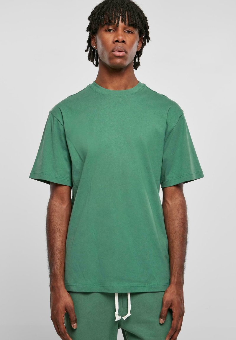 Tricou verde cu mânecă scurtă, fabricat din bumbac, cu decolteu rotund. Prezintă o croială confortabilă și o textură netedă, purtat împreună cu pantaloni asortați.