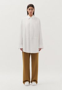 Witte oversized blouse met een kraag en lange mouwen, gecombineerd met bruine wijde broek en witte sneakers. Eenvoudig, schoon ontwerp.