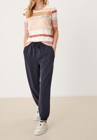 Top de manga corta a rayas en crema, naranja y rojo; combinado con pantalones navy con cordón; zapatillas blancas con cordones y acentos negros.