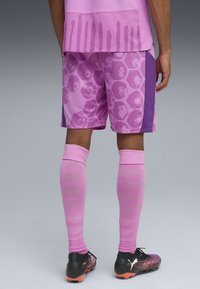 Rosa sportshorts med hexagonmönster, kombinerat med rosa knästrumpor och svarta fotbollsskor med en gradientdesign.