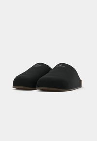 Melni slip-on clogi ar gludu matētu apdari, noapaļotu purngalu, diskrētu logotipu augšpusē un brūnu teksturētu zoli labākai saķerei.