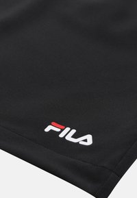 Tissu noir avec un logo FILA blanc et rouge imprimé près du bord cousu, montrant un gros plan du textile et des détails du logo.