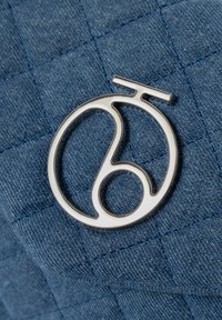 Hopeapintalogo tekstuurilla varustetulla sinisellä kankaalla, jossa on palaset. Pinnassa on pyöreä muotoilu ja pieni vaakasuora palkki ylhäällä.