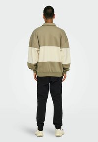 Olive green and cream oversized sweatshirt with a crew neck, drop shoulders, ribbed cuffs, and heathered texture. Worn with black pants.