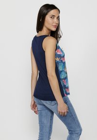 T-shirt sans manches navy avec impression florale sur le devant, teintes bleues et roses, texture douce et ourlet arrondi. Porté avec un jean bleu clair.