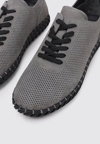 Zapatillas grises perforadas con cordones negros y una suela de goma texturizada, que cuentan con un diseño elegante y una estética casual.