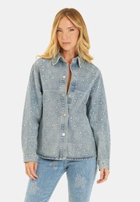 Veste en denim bleue ornée d'un motif paisley et de détails en argent, avec un col et une fermeture à boutons-pression.